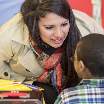 A student teacher smiles at an elementary student in a classroom