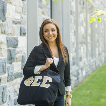 A woman stands with her bag that has greek sorority letters on it