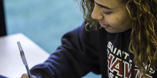 A woman in a HAWKS sweatshirt writes in her notebook.