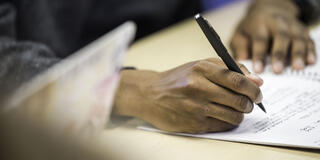A person's hands are shown writing with a pen on a piece of paper