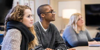 3 students looking at professor in the communication lab