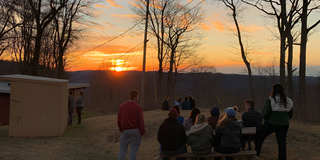 A group of students sitting outside at a picnic table watching the sun set