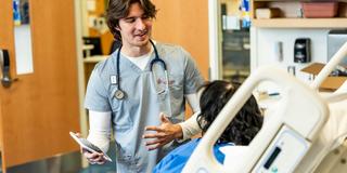 Nursing student speaking with a patient while holding a tablet