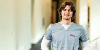 Male nursing student wearing gray scrubs standing in hallway