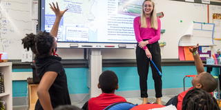 A teacher and two elementary students raising their hands in a classroom 