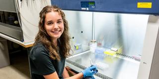 McNulty Scholar sitting in front of a hood with a pipett_Biology Lab
