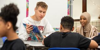 Male student teacher reading to group of students