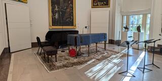 a piano set up in an art gallery with light streaming through the windows