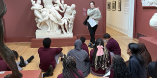 Students seated in front of the Laocoon sculpture. An educator is teaching. 