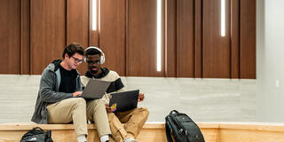 Two students sitting down and looking at a laptop