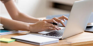 female student's hands typing on laptop