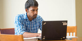 male graduate student typing on a laptop