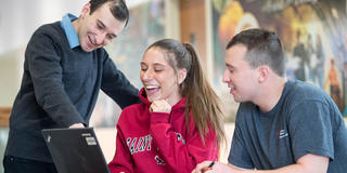Faculty member teaching two students in front of laptop