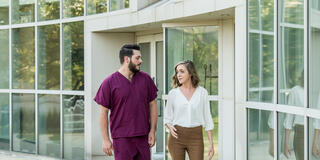 A young man in scrubs and a young woman in professional clothing walk across campus