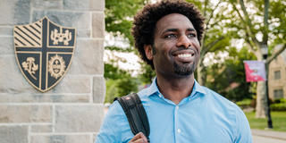 Jameel smiles in front of a stantion with the SJU seal on it