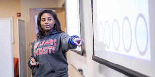 female student wearing a saint joseph's university hoodie, pointing at a screen