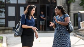 Two adult students smile at each other as they talk outside the student center on campus