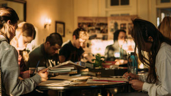 A group of students sitting at a long table looking down at books