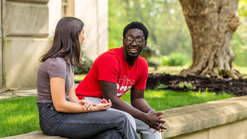 Male and female student sitting outside on a curb and talking