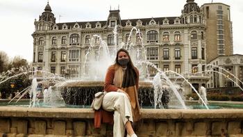 Christina Photiades sitting on a water fountain in front of a building in Spain.