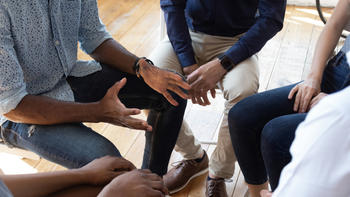 A closeup of hands in a circle, perhaps in a recovery group meeting