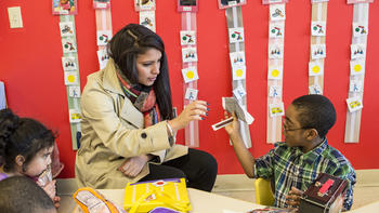 A student sits with a young child, teaching him something