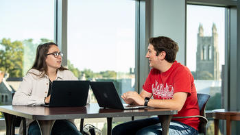two saint joseph's university students talking to each other while on their laptop
