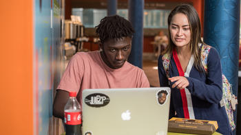 A student helps another student as he works on a laptop