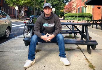 Noah Henderson in a hat and sweatshirt sitting on a picnic table