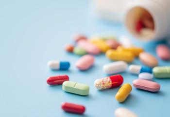 Colorful pills scattered from white plastic pill bottle on blue background