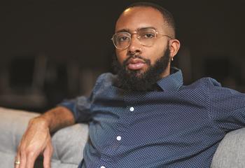 Alumnus Joseph Thomas seated on a gray couch with his arms back