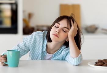 Tired woman leaning on counter drinking coffee