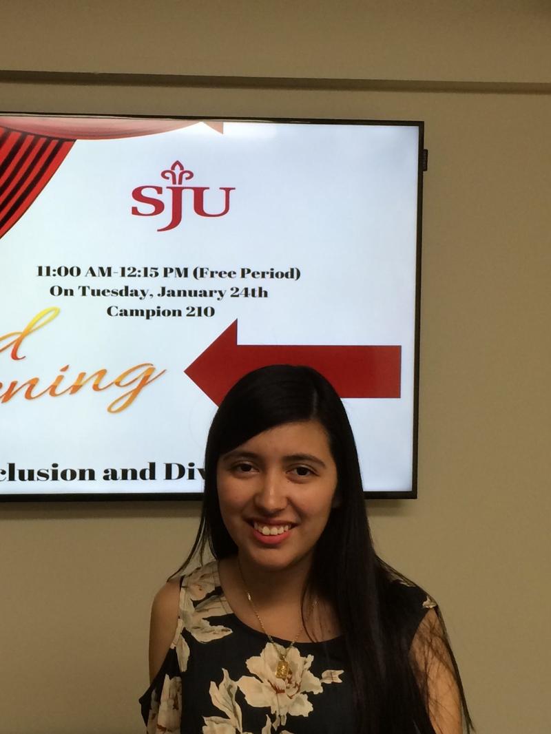 a girl with dark hair, standing in front of a TV screen and smiling at the camera