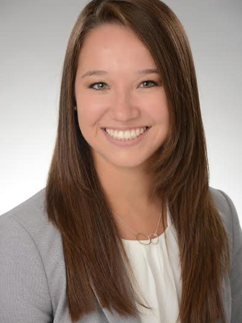 a girl with brown hair and a gray blazer, smiling at the camera