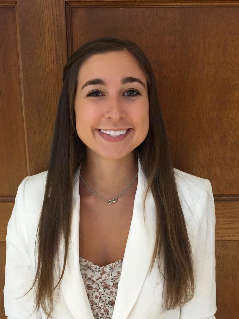 a girl with brown hair and a white blazer, smiling at the camera