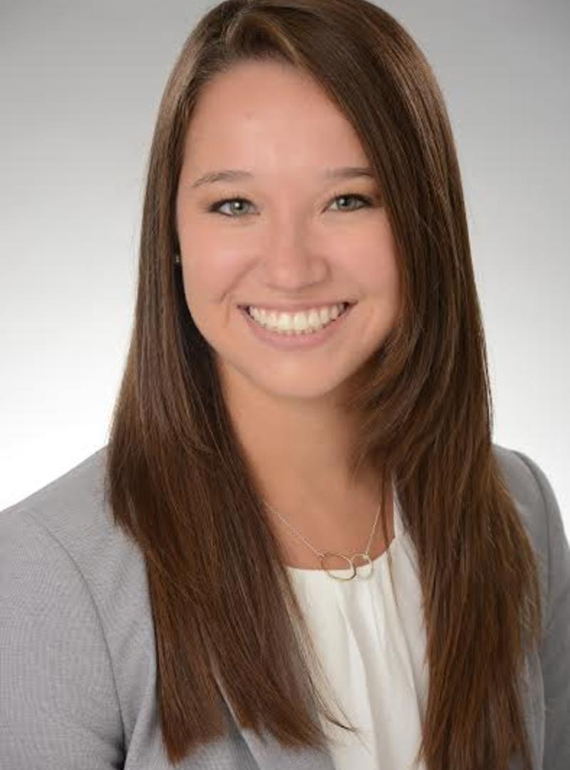 a girl with brown hair and a gray blazer, smiling at the camera