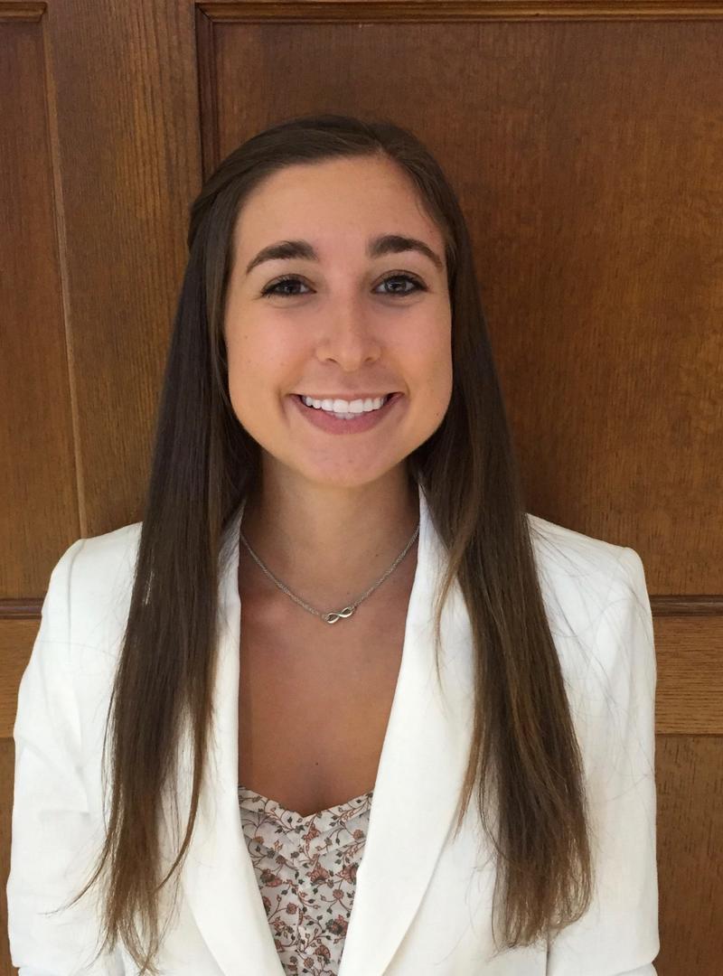 a girl with brown hair and a white blazer, smiling at the camera