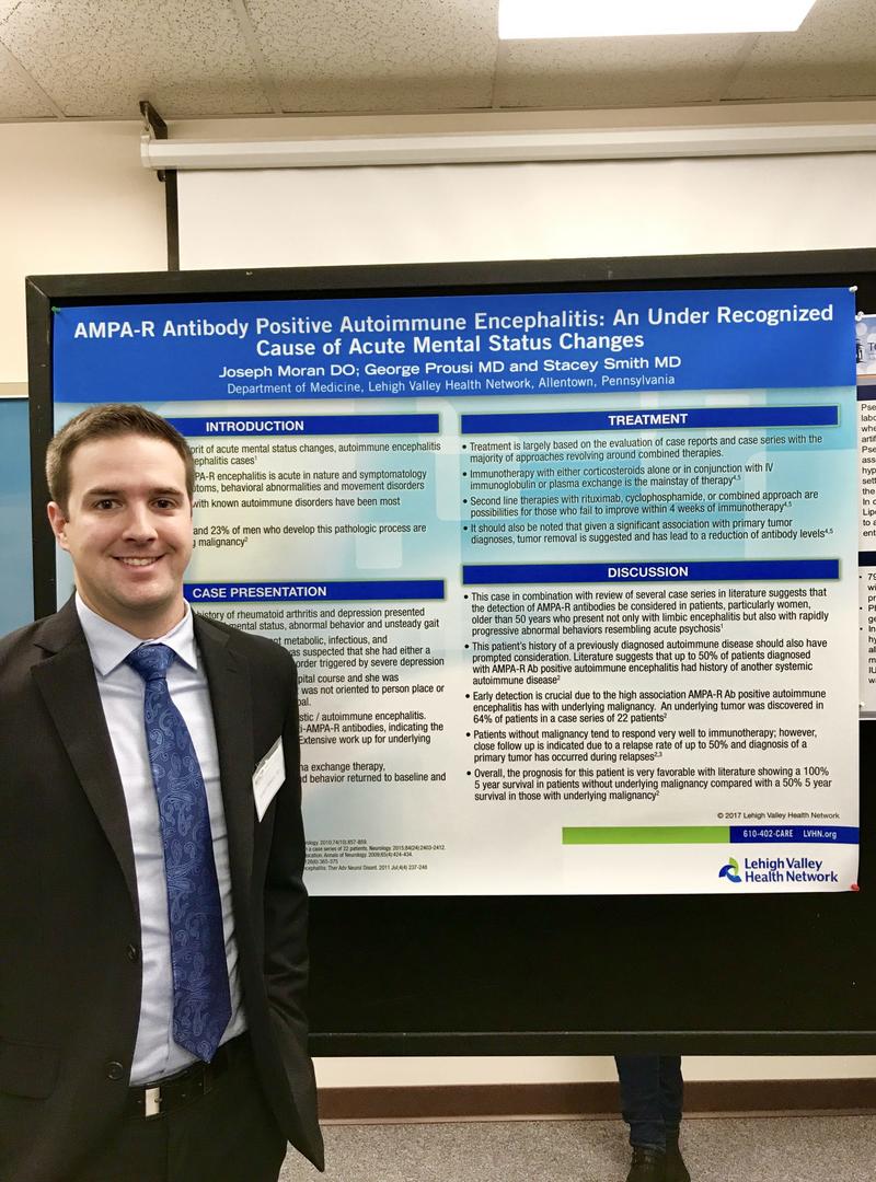 a young man wearing a suit and standing in front of a science research poster