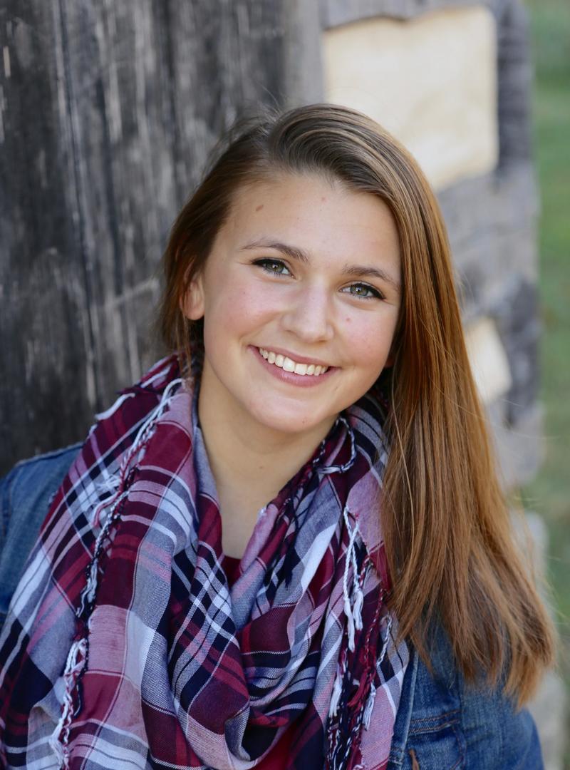 a young woman with light brown hair wearing a scarf and smiling at the camera