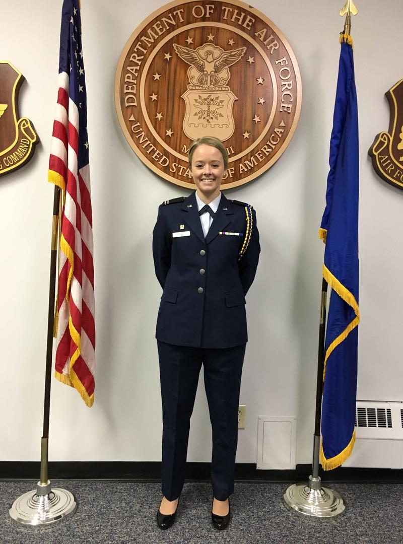 a young woman dressed as a cadet and standing in between two flags