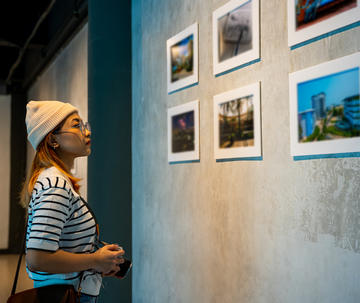 Woman with a camera looking at pictures on gallery wall