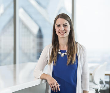 A student in a business casual outfit stands with a skyscraper behind her