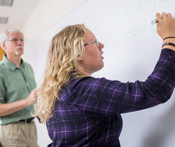 student writing on a white board with professor standing next to her