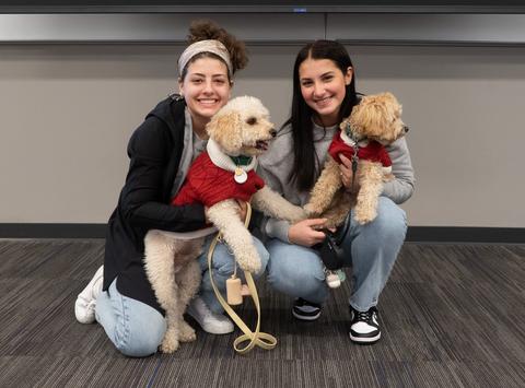 Two female students kneel down with their dogs