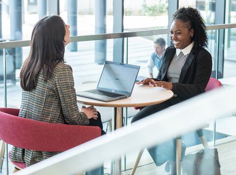 2 females sitting at table together with a laptop open