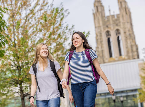 two saint joseph's university students walking outside, on campus, with barbelin hall tower behind them