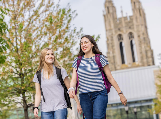 two saint joseph's university students walking outside, on campus, with barbelin hall tower behind them