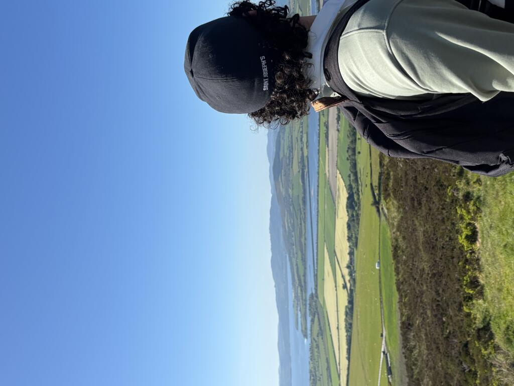 The back of a student who's hat reads "Saint Joseph's University" and the student is overlooking a green field.