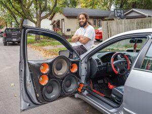 man siting on hood of car with large speakers in door