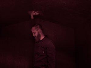 bearded man pressing hand to ceiling of storm shelter